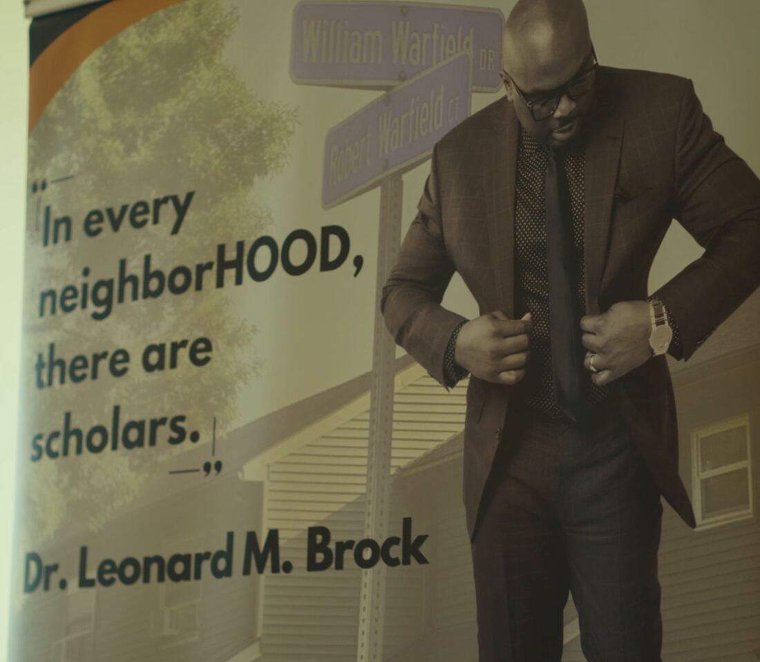The NeighborHOOD Scholar banner reading &ldquo;In every neighborHOOD, there are scholars,&rdquo; with Dr. Leonard M. Brock beside the William Warfield Drive street sign